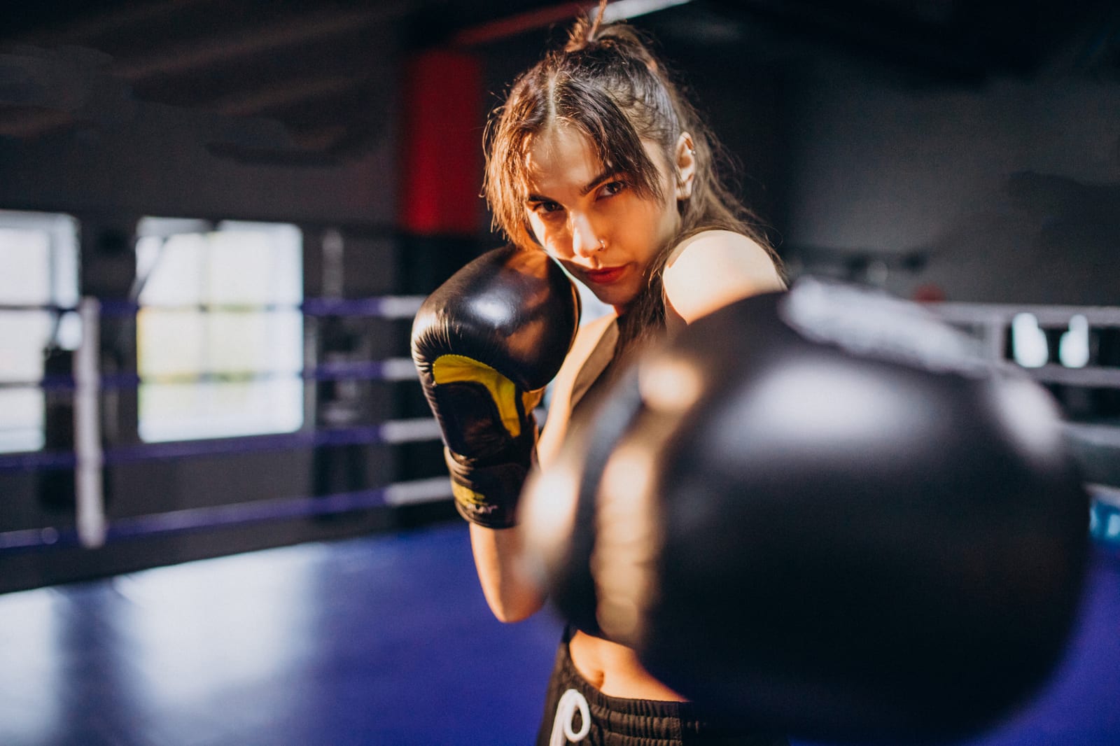 A woman in boxing gloves extending a punch toward the camera inside a ring.