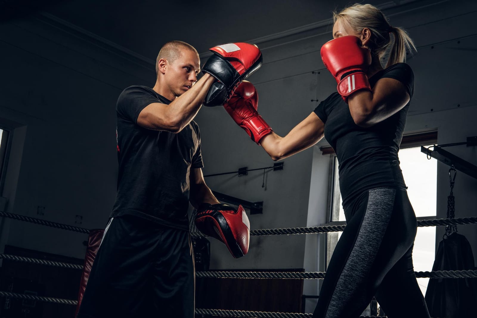 A trainer holding focus mitts while a student punches at the edge of a ring.