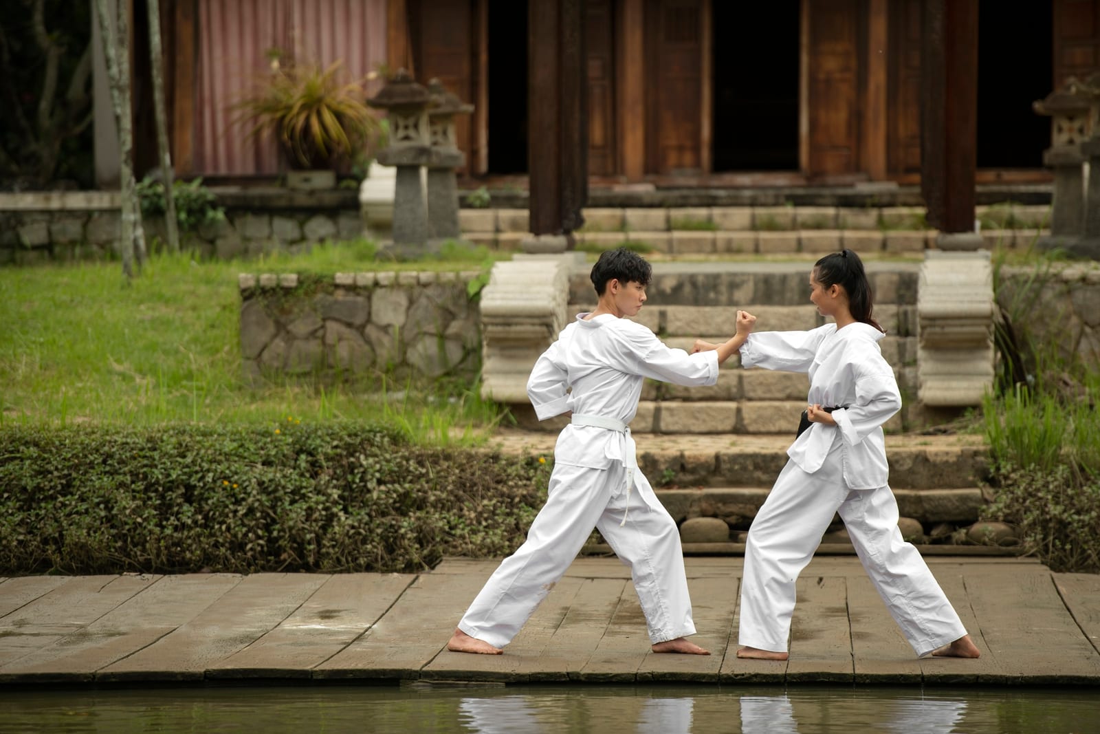 Two martial artists in white gis drilling blocks on a path in front of a temple.