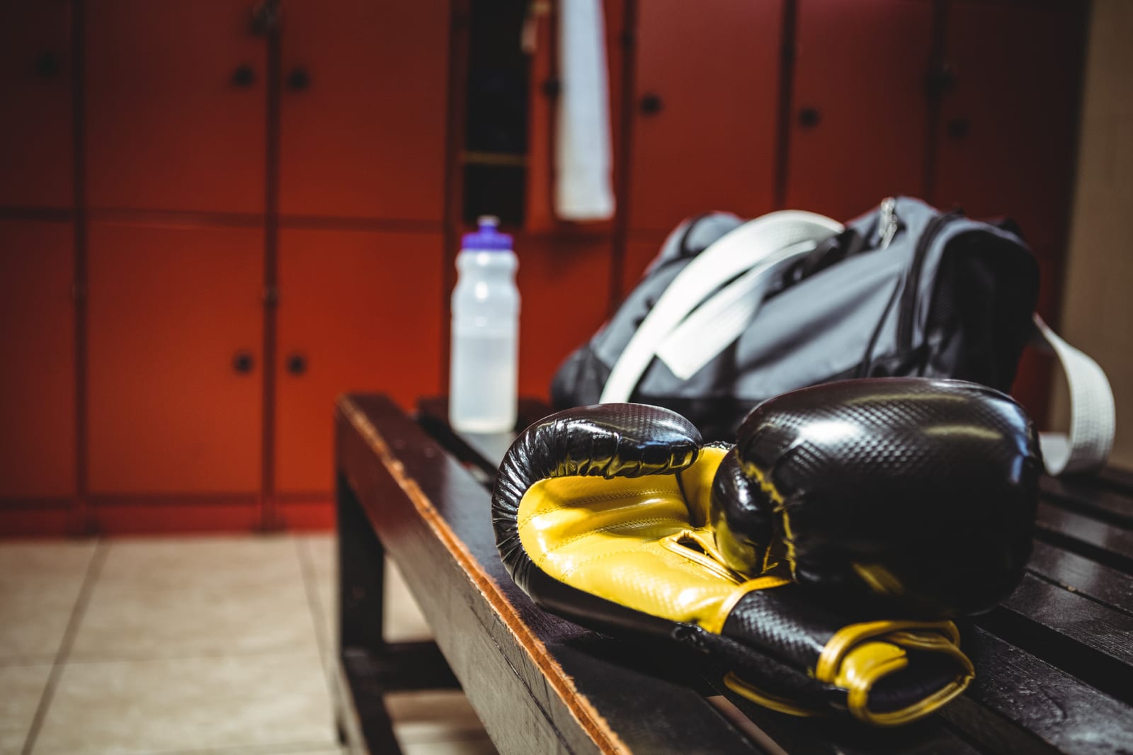 Boxing gloves, a gym bag and a water bottle resting on a bench in a changing area.